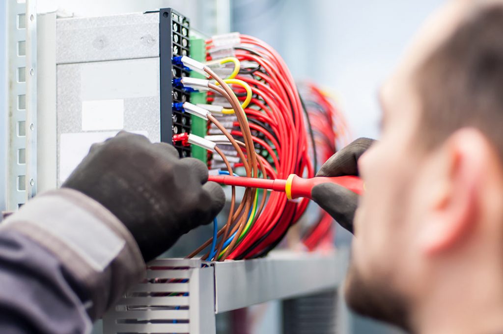 Nahaufnahme eines Elektrikers bei der Arbeit an elektrischen Kabeln und Leitungen.