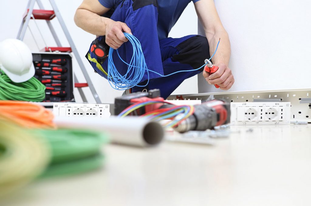Elektriker schneidet mit einer Zange ein Stromkabel und arbeitet an der Installation elektrischer Leitungen.